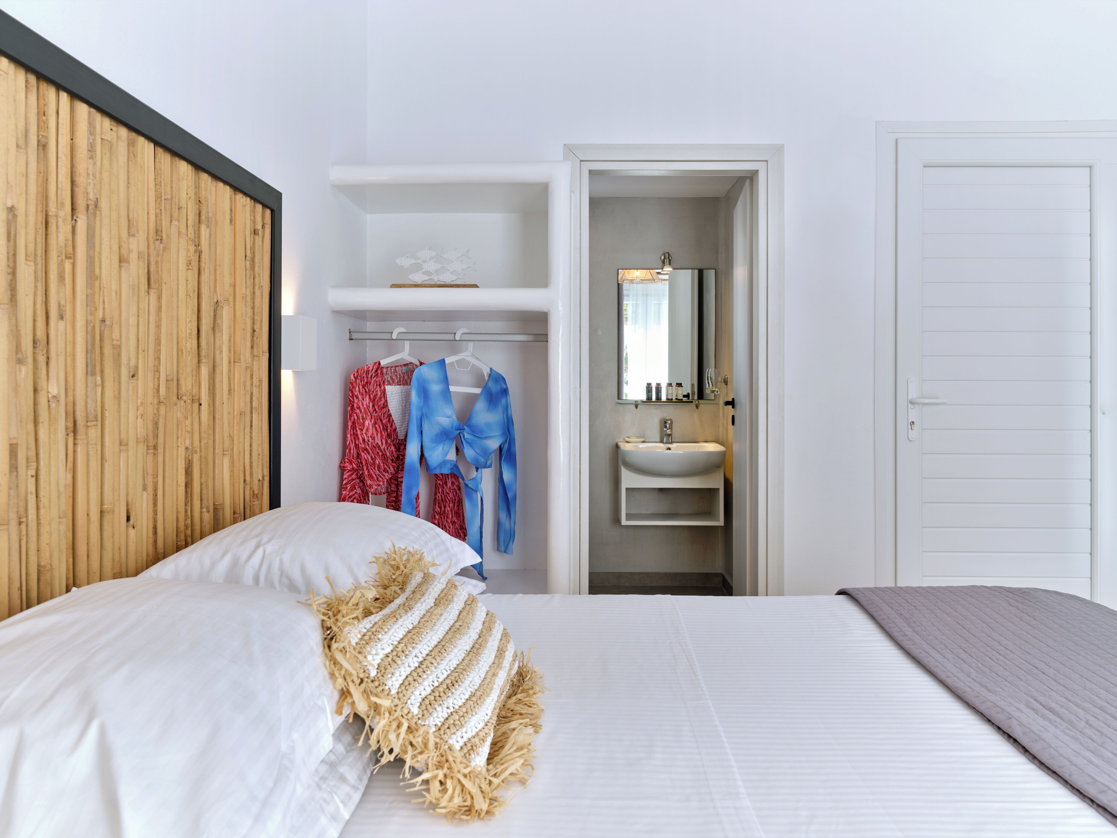 A bedroom with a bed, a bedside table, a mirror, a wardrobe, and a bathroom with a sink.