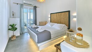 Una habitación de hotel moderna con una cama grande, una mesita de noche con una botella y vasos, una pequeña planta y vistas al exterior.