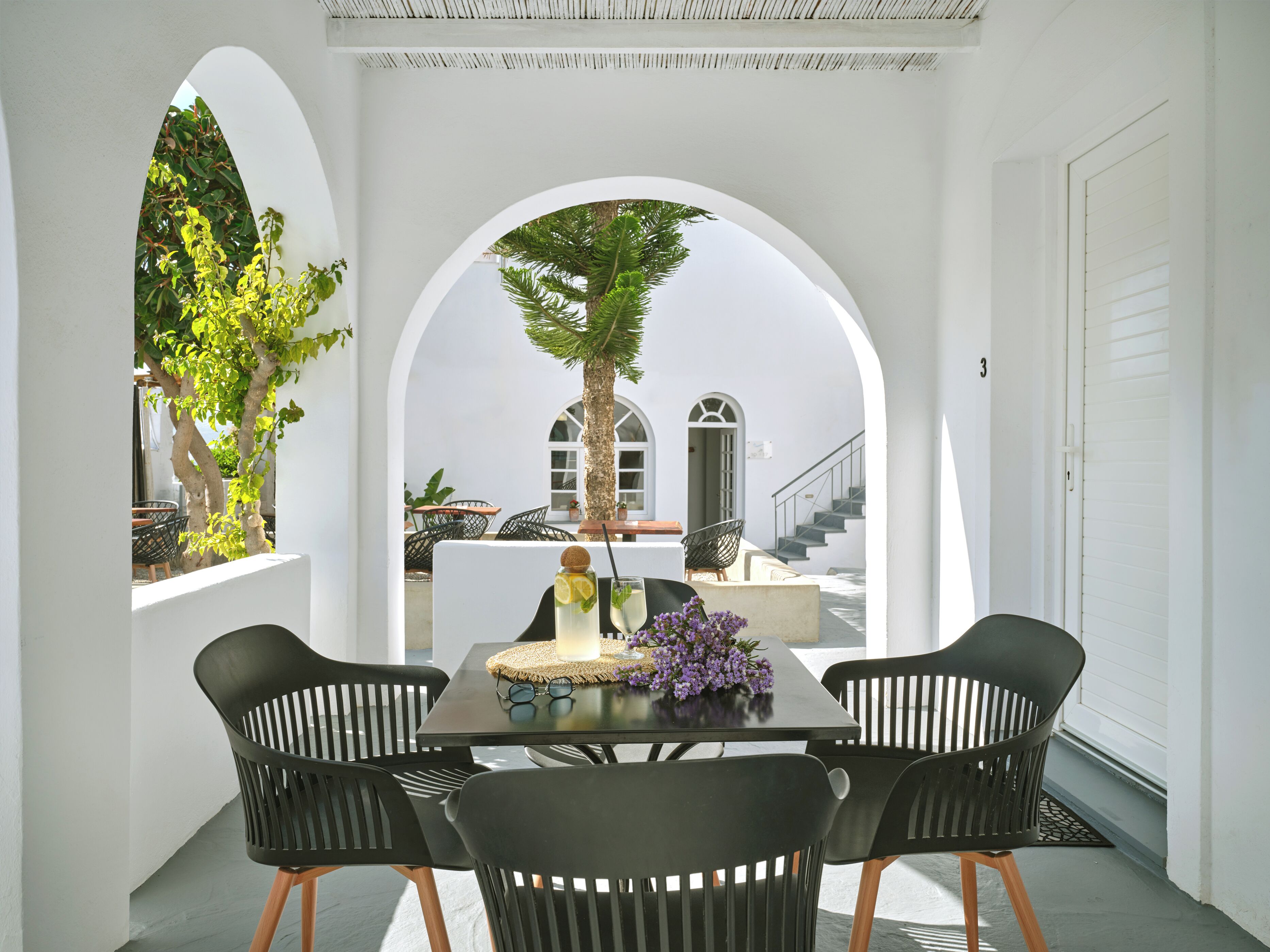 A dining area with a table and four chairs, a potted plant, and a view of a staircase and balcony.