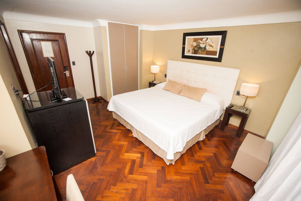 A hotel room with a large bed, a desk with a computer, a wardrobe, and a framed picture on the wall.