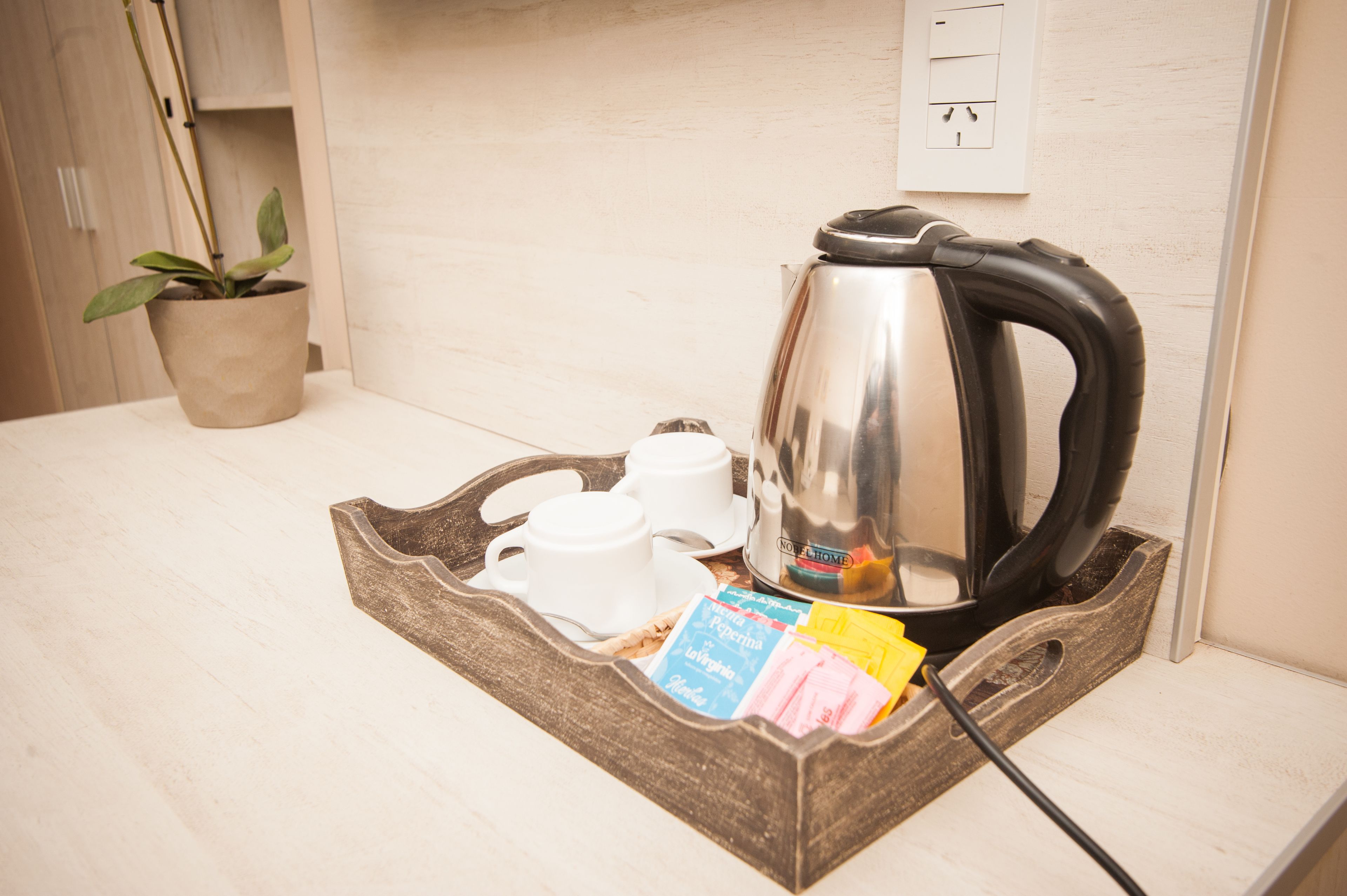 A kitchen area with a kettle, two cups, a tray, and a potted plant.