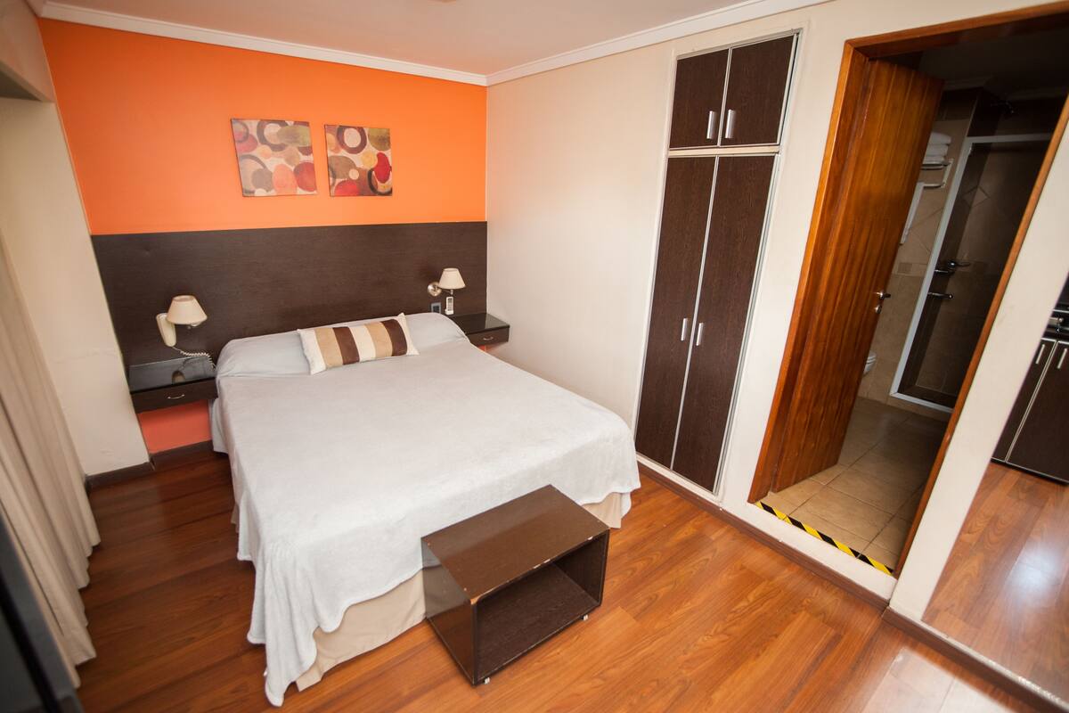 A bedroom with a bed, nightstands, a wardrobe, and a bathroom visible through an open door.
