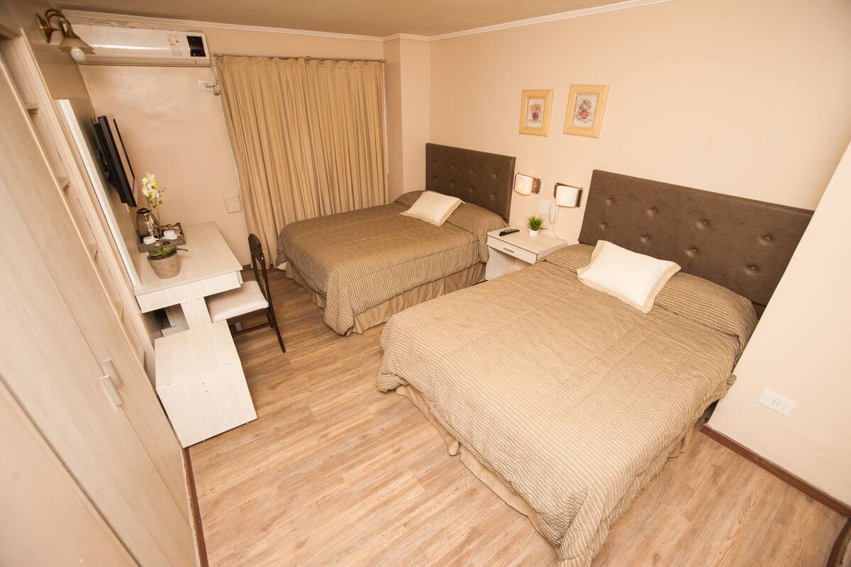 A hotel room with two beds, a desk, a chair, a TV, and a window with curtains.