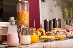 A breakfast buffet with various food items and beverages, including a pitcher of milk, a pitcher of orange juice, and a large container of cereal.
