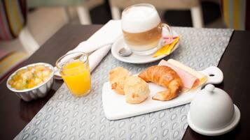 Desayuno con una taza de café, croissants, jamón y queso, y un bol de fruta sobre una mesa.