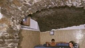 Habitación con paredes de piedra, una bañera de hidromasaje de madera y un banco de madera.