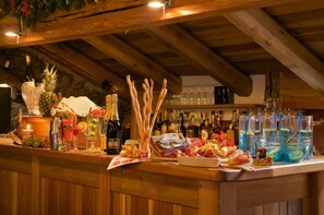 A bar area with wooden beams, a variety of bottles, glasses, and a selection of fruits and snacks. - Chalet Faure (Sauze d'Oulx)