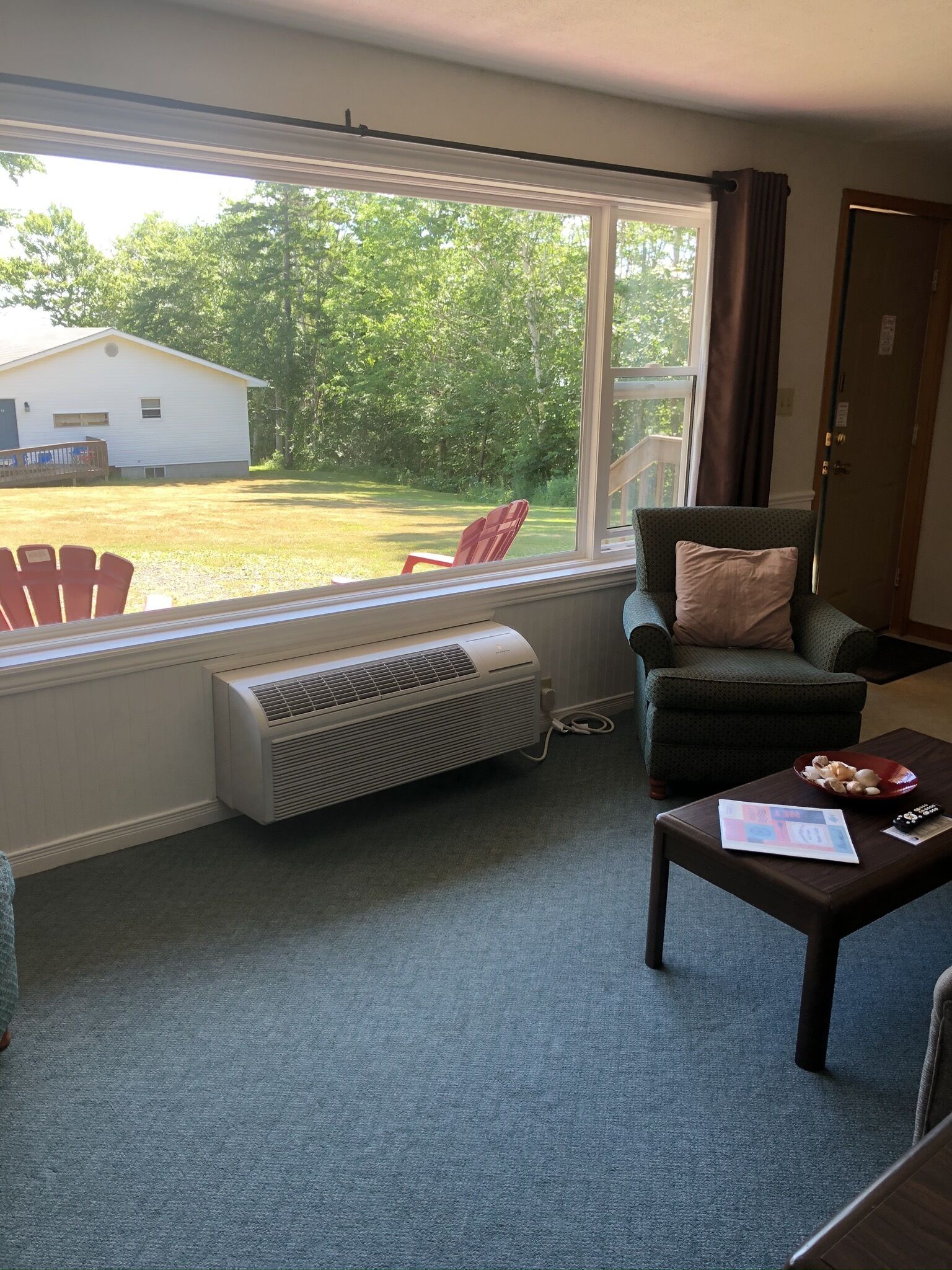 A room with a large window, a chair, a couch, a table with a remote control, and a heater.