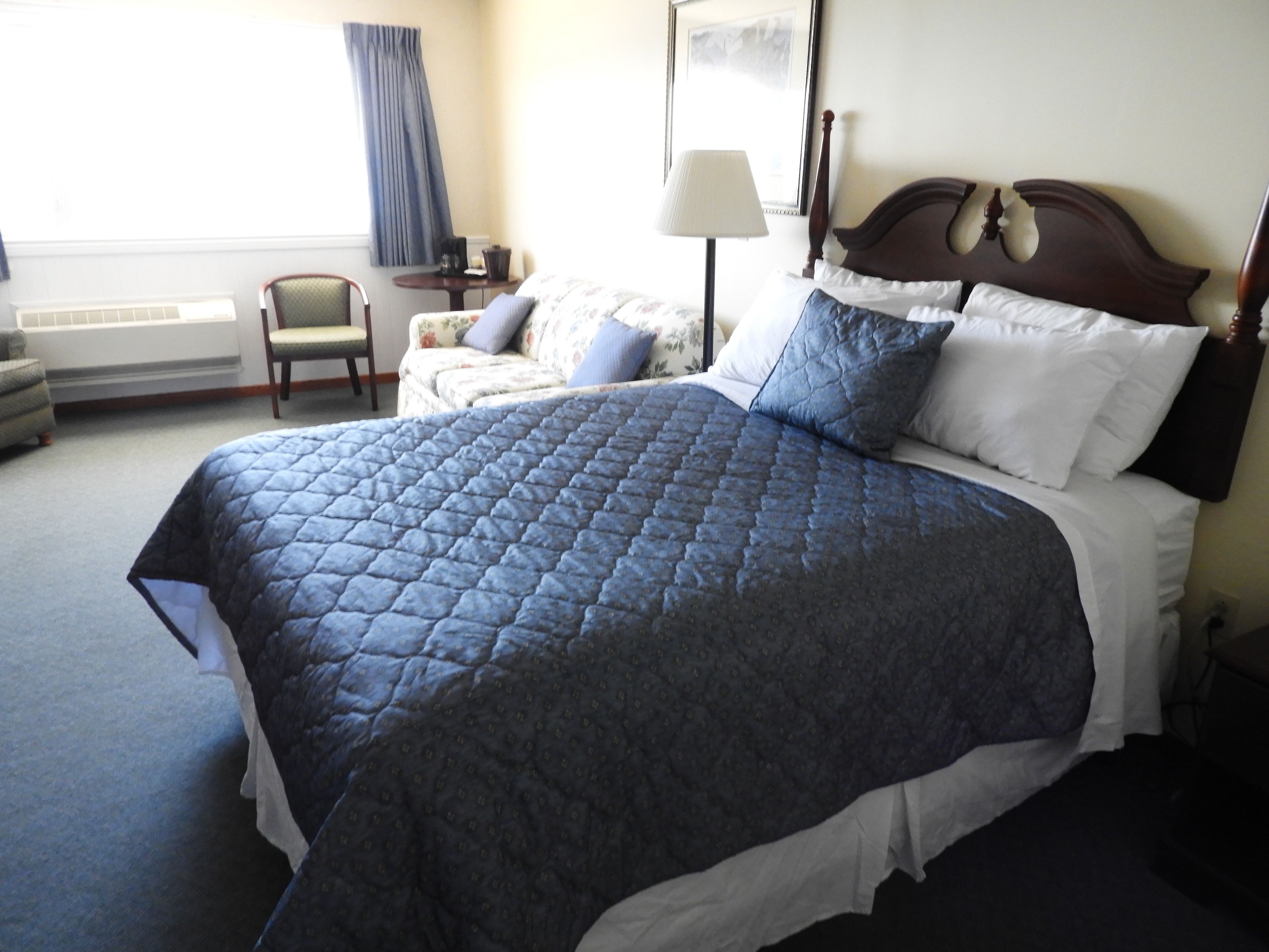 A neatly made bed with a blue quilt, a wooden headboard, and a bedside table with a lamp.