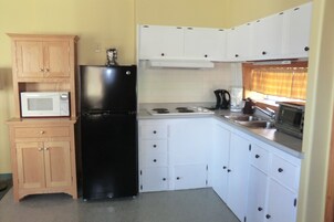 A compact kitchen with white cabinets, a black refrigerator, a microwave, a stove, and a sink.