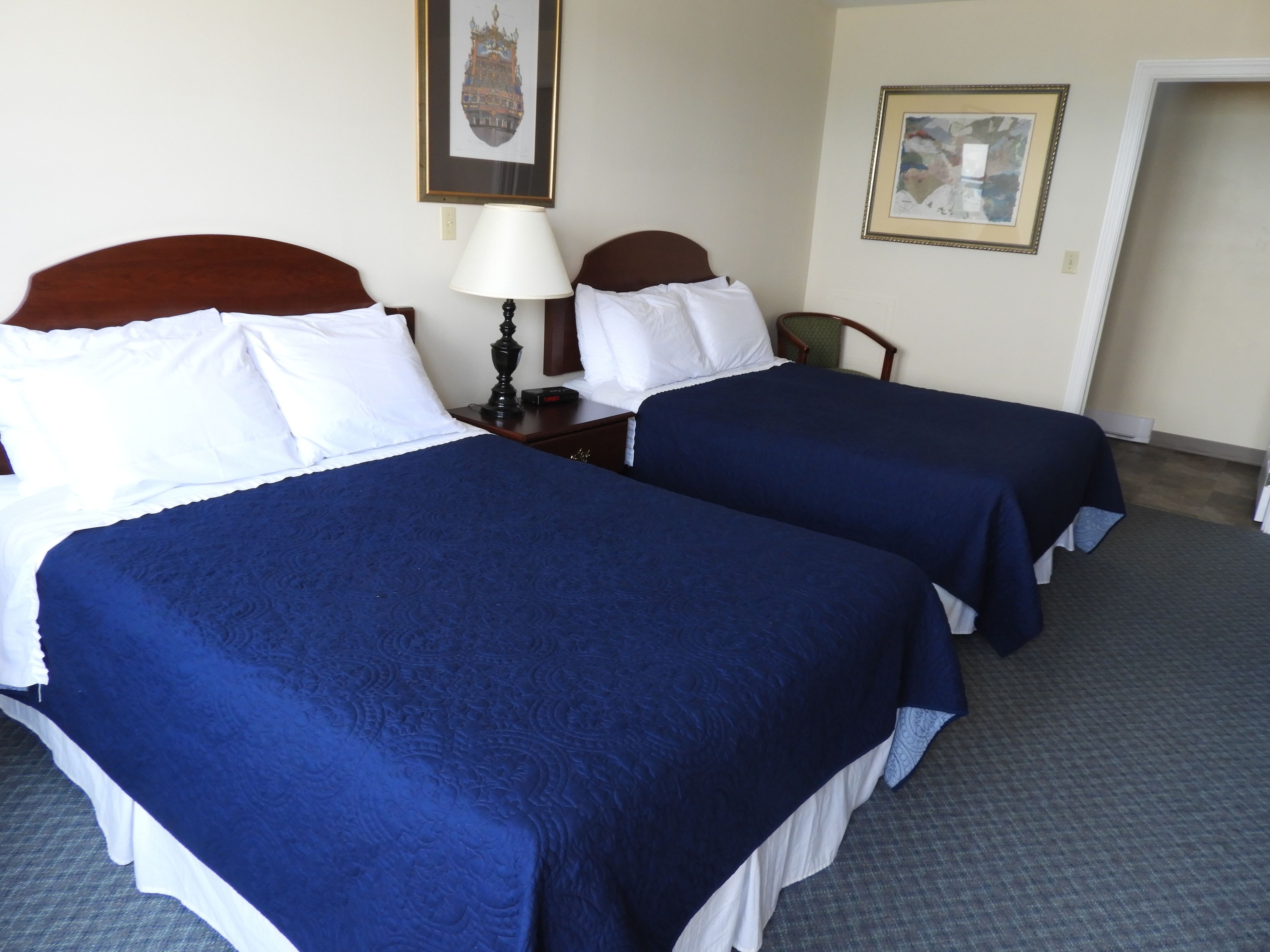 Habitació d'hotel amb dos llits, una taula de nit, una làmpada i dos quadres a la paret.