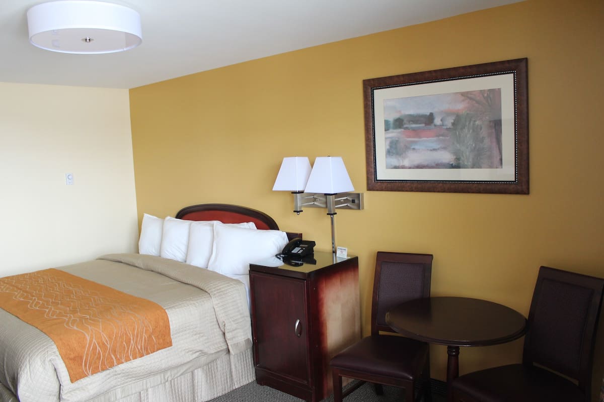 A hotel room with a bed, bedside table with lamps, a small desk, and a chair.