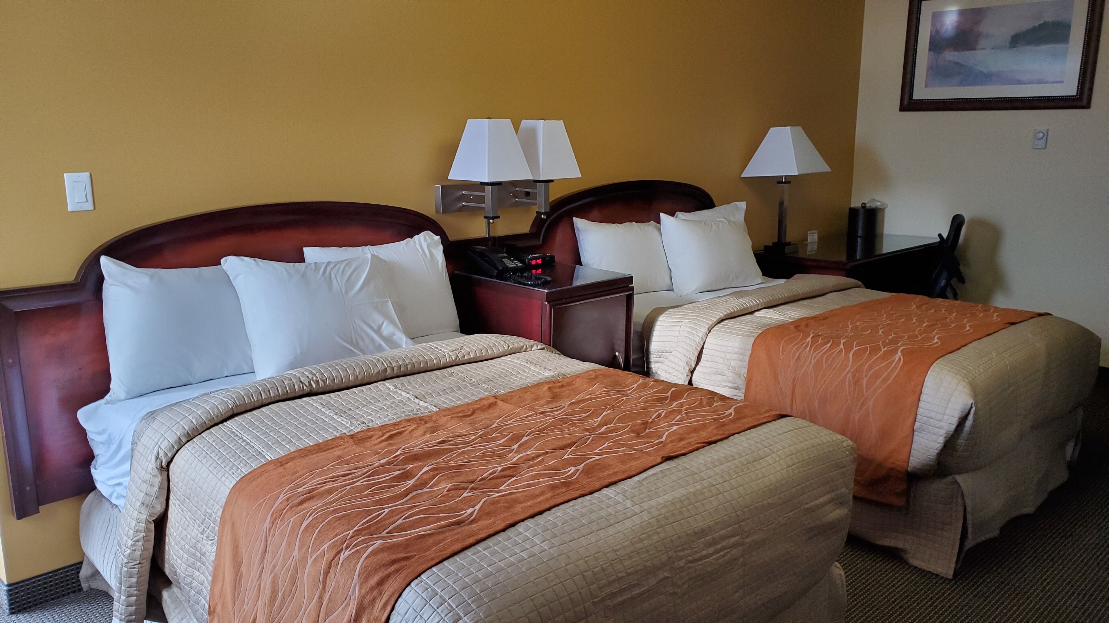 Habitación de hotel con dos camas, cada una con cabecera, mesitas de noche, lámparas y teléfono.