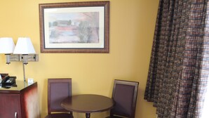 A hotel room with a round table, two chairs, a desk with a phone, a framed picture on the wall, and a plaid curtain. - Imperial Fireside Inn (Sudbury)