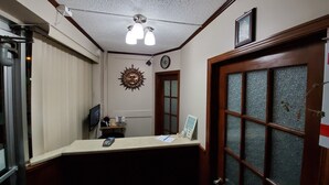A reception area with a desk, a clock, a decorative sunburst wall piece, and a frosted glass door. - Imperial Fireside Inn (Sudbury)