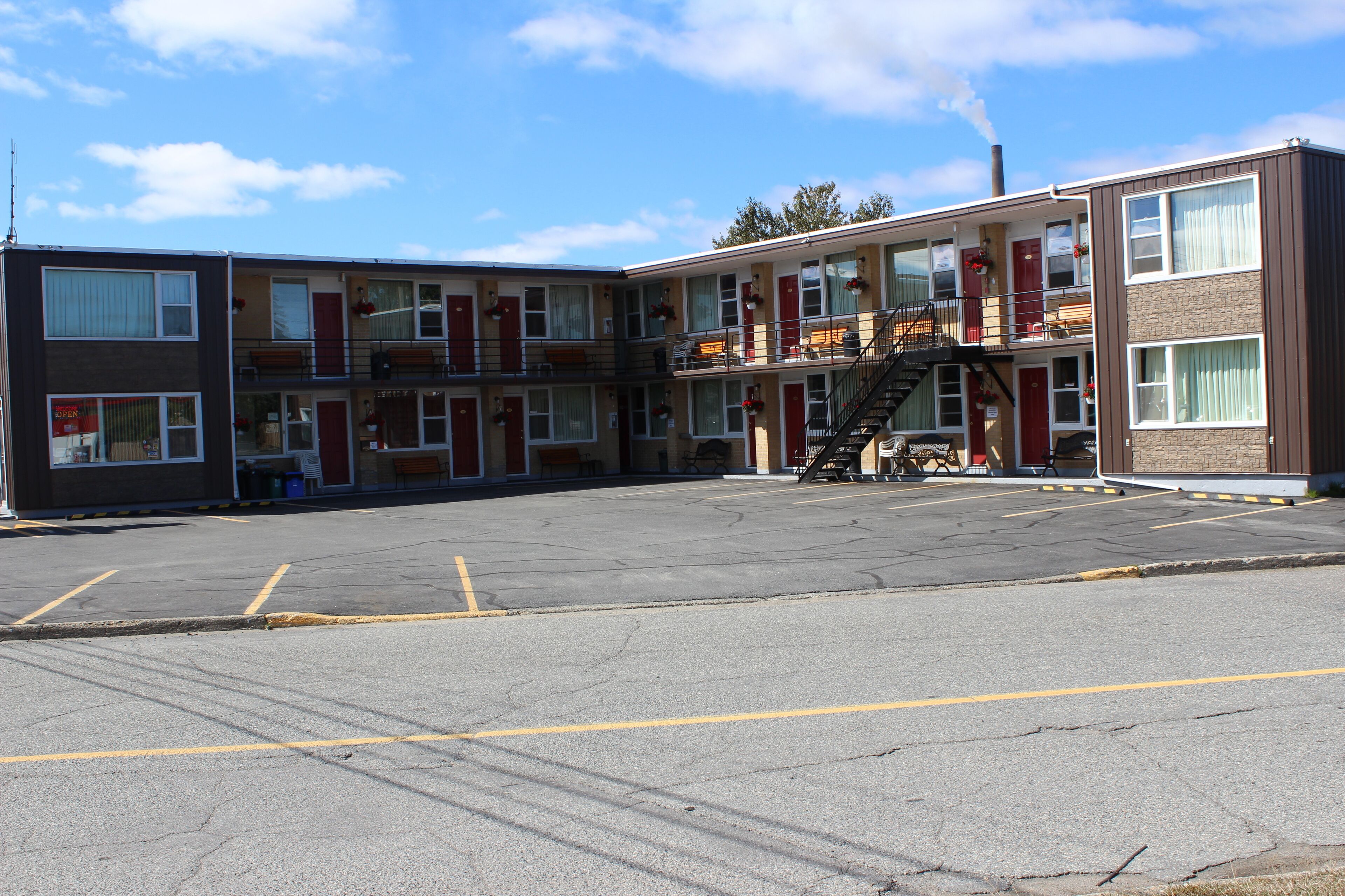 A multi-story motel with a central staircase, individual rooms on each floor, and a parking lot in front.