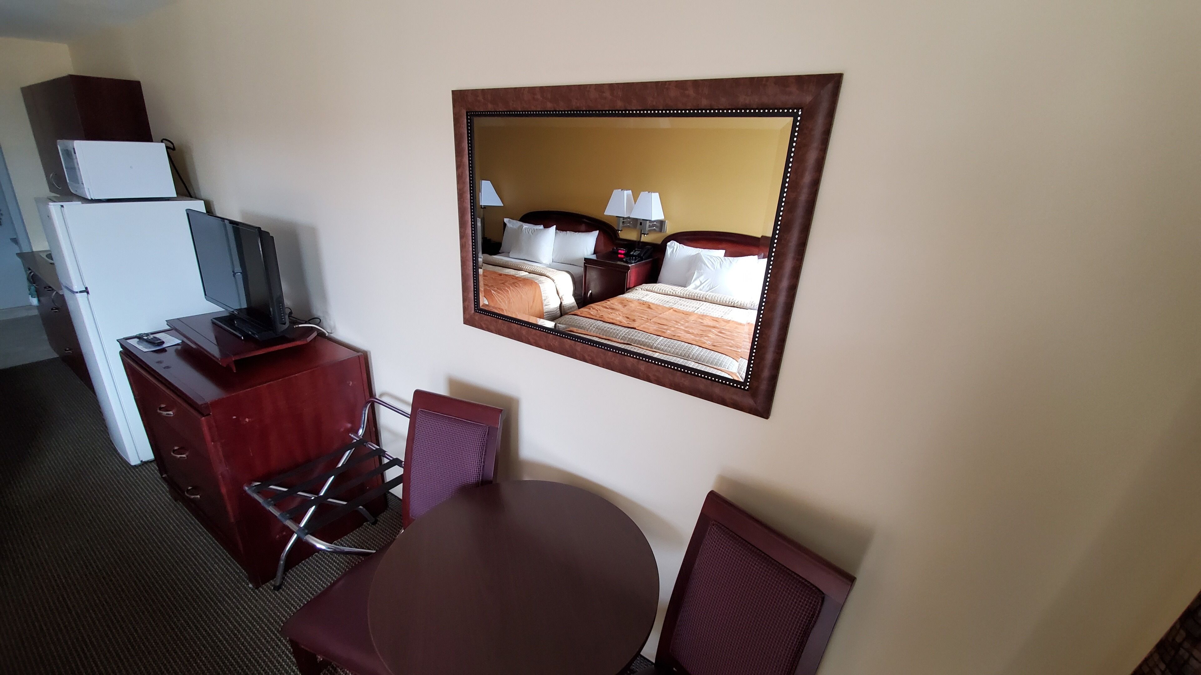 A hotel room with a bed, a desk with a computer, a chair, a table, and a mirror.