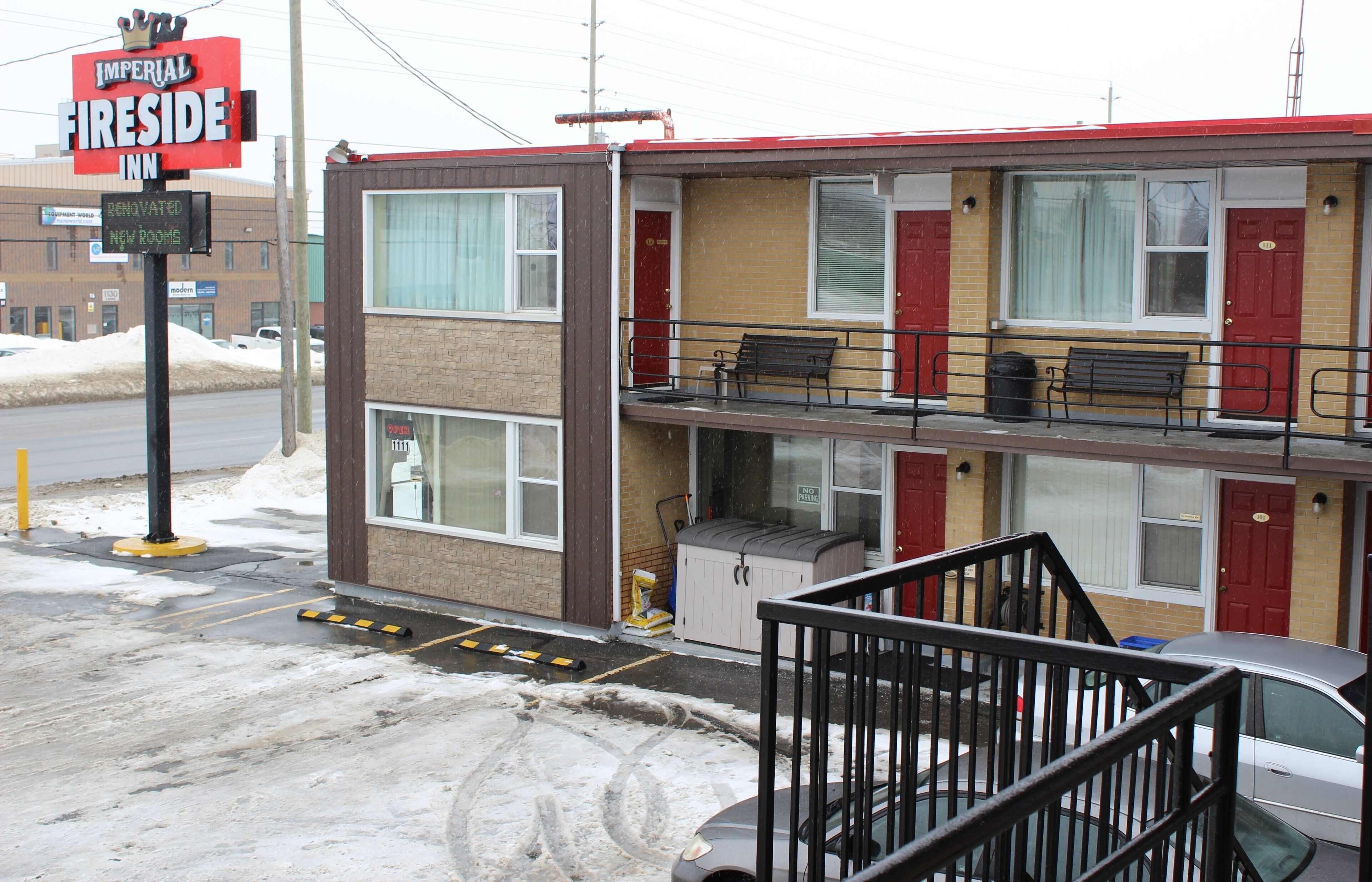 A motel with a red roof, two-story structure, and a balcony with benches.