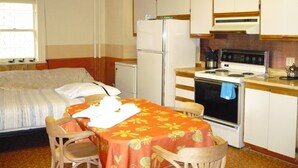 A compact room with a bed, a small table with chairs, a kitchenette with a stove and refrigerator, and a window with blinds. - L'Intendant (Québec City)