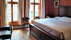 A hotel room with a large bed, a chair, a desk, and a window with curtains. - L'Intendant (Québec City)