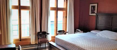 A hotel room with a large bed, a chair, a desk, and a window with curtains.