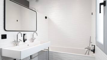 Un baño moderno con un lavamanos blanco, dos grifos, un espejo grande y una bañera.