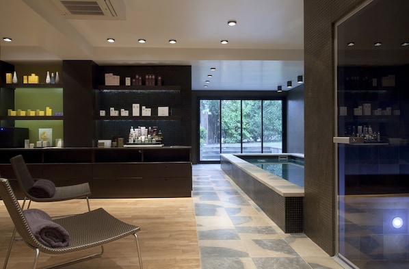 A modern spa area with a relaxation chair, a reception desk, a pool, and a view of the outdoors.