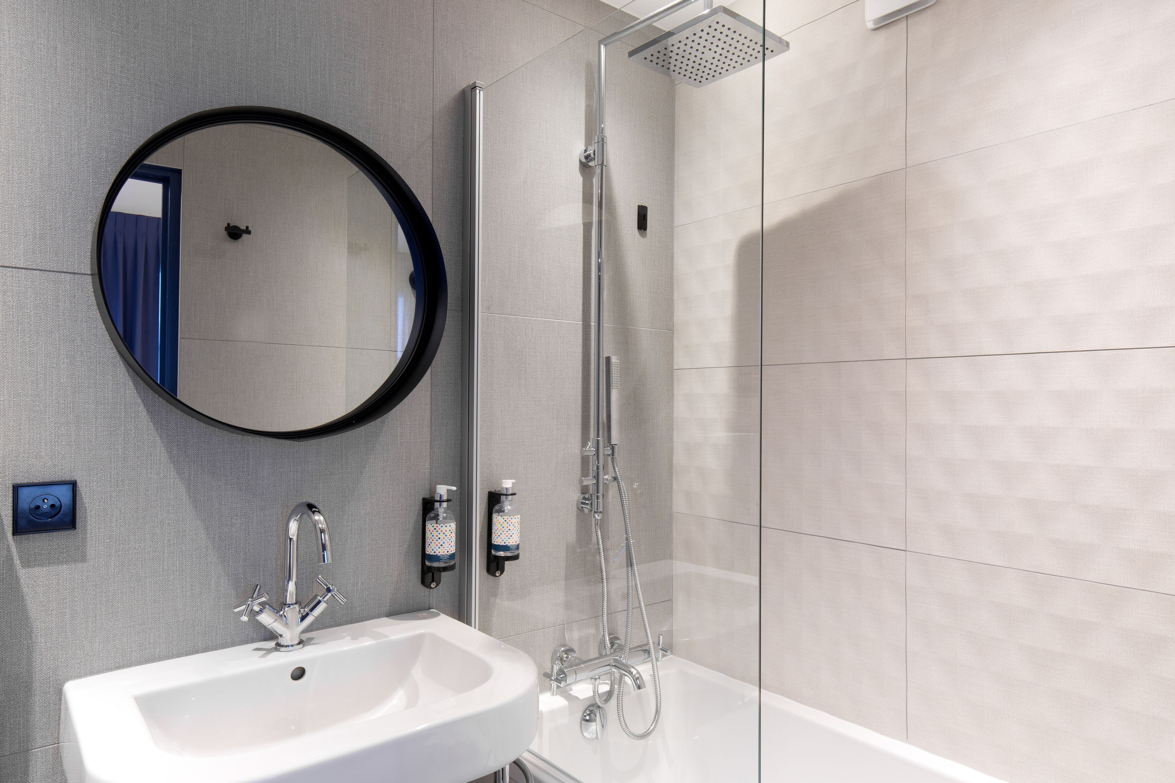 A modern bathroom with a white sink, a round mirror, and a glass-enclosed shower.