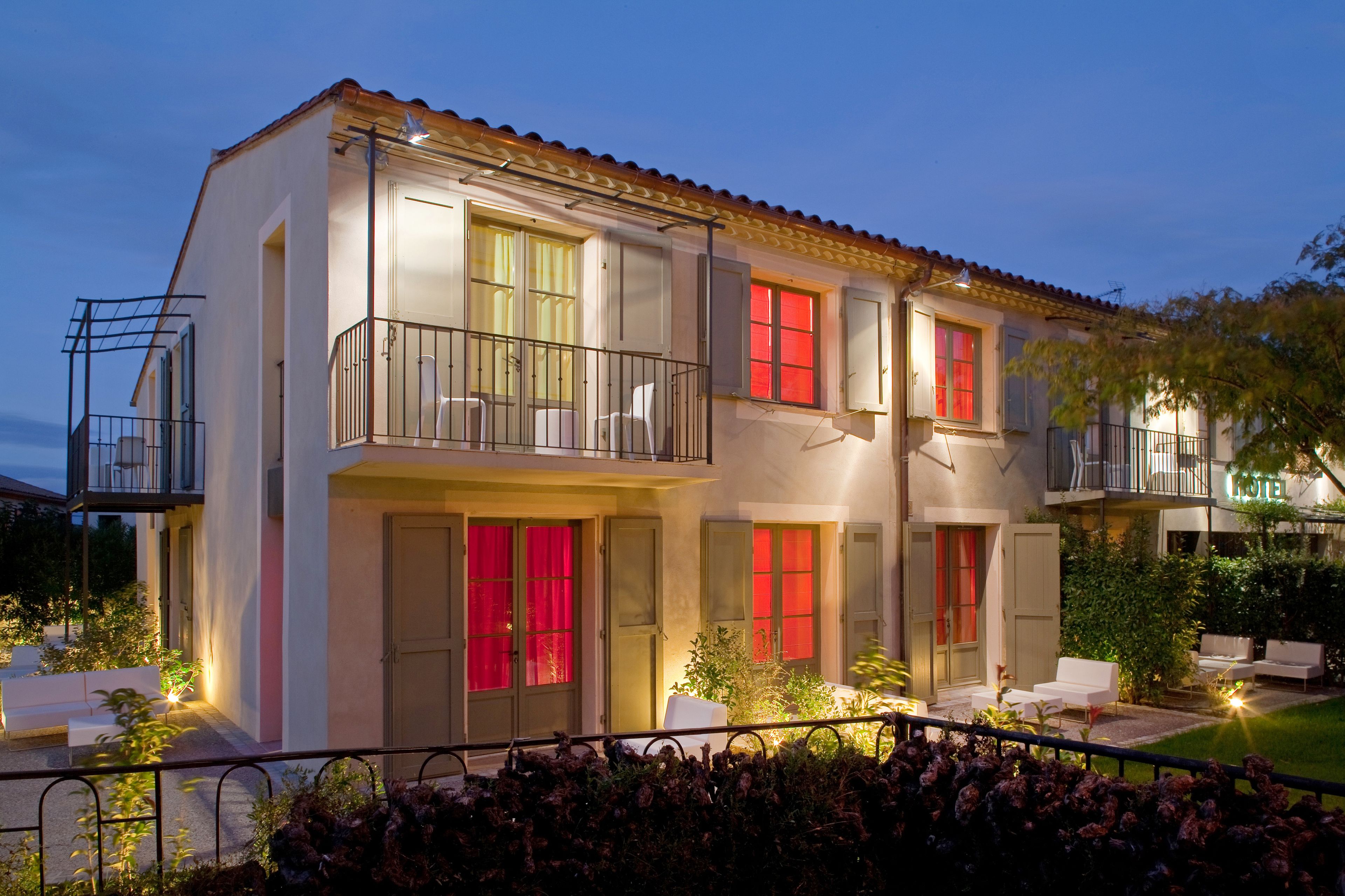 Un bâtiment à deux étages doté d’un balcon, d’un espace extérieur aménagé pour s’asseoir et d’un jardin bien éclairé.