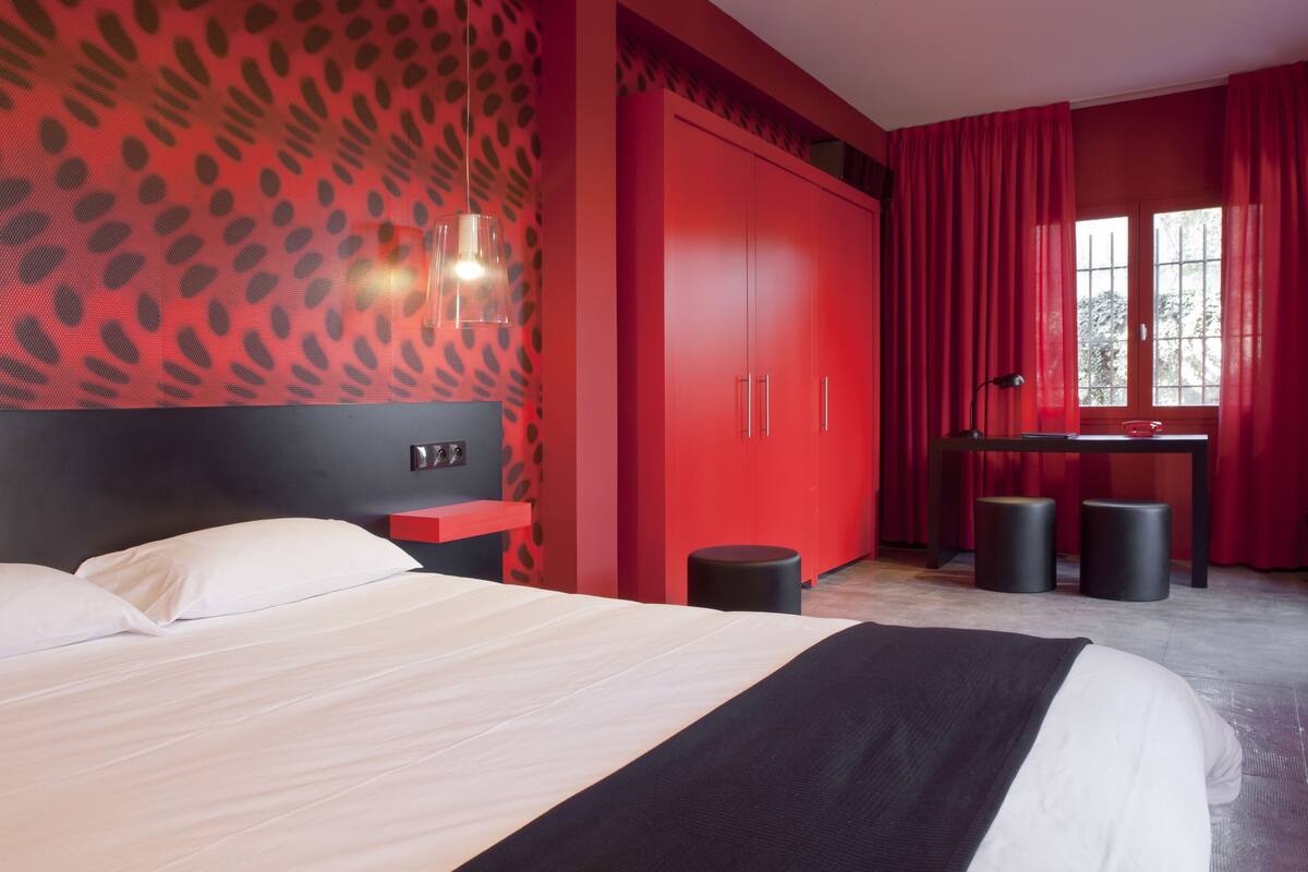 Ein modernes Schlafzimmer mit einem großen Bett, einem roten Kleiderschrank und einem Schreibtisch mit zwei Hocker.
