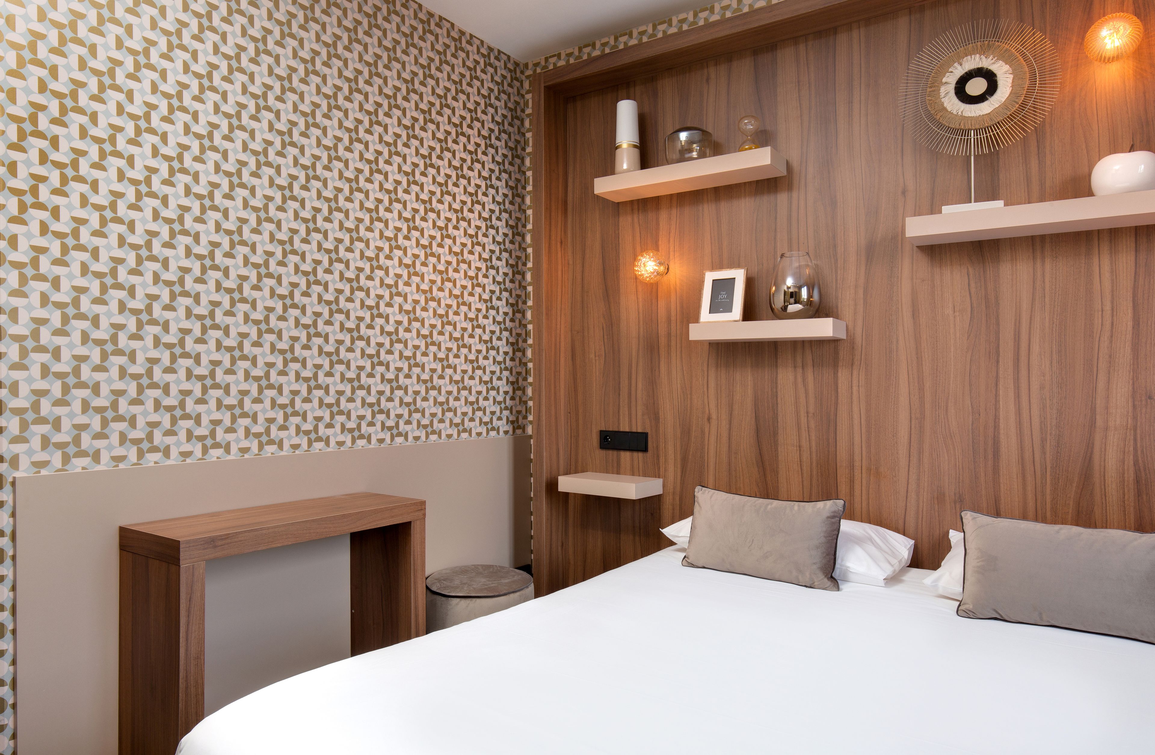 A modern bedroom with a geometric patterned wall, wooden paneling, and built-in shelves with decorative items.