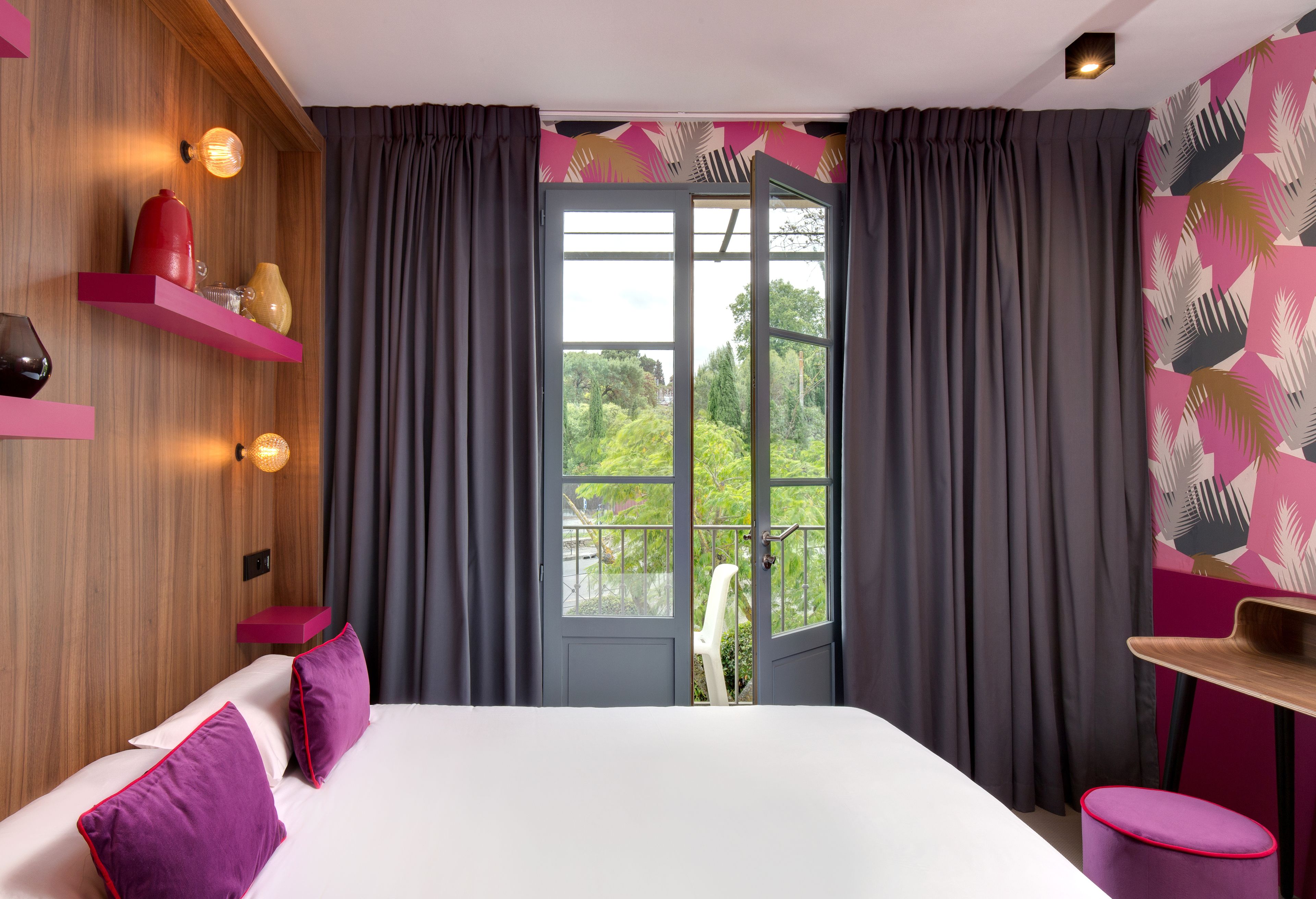 Habitación de hotel moderna con una cama, una silla, una mesita y vistas a zonas verdes a través de una puerta.