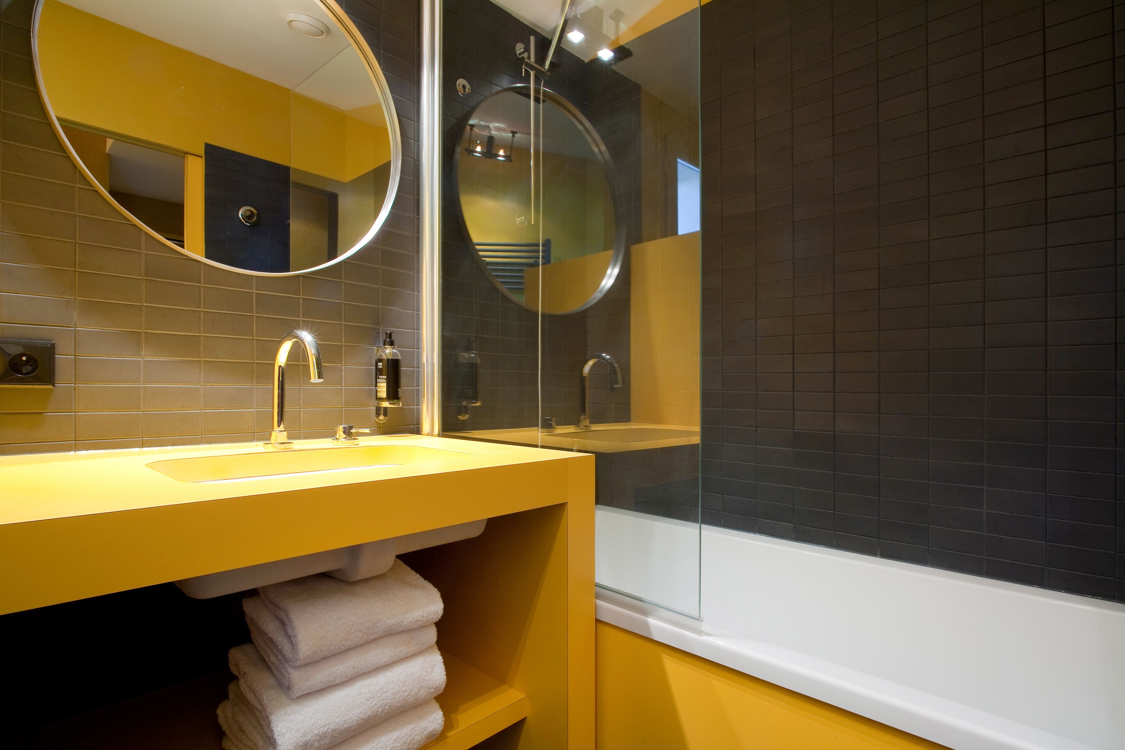 Une salle de bain moderne avec un lavabo jaune, deux miroirs et une baignoire.