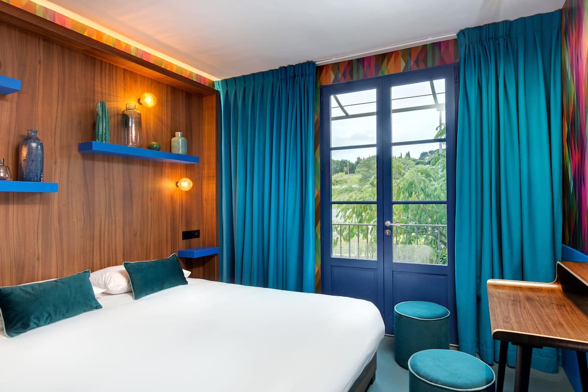 Ein Schlafzimmer mit einem Bett, zwei blauen Stühlen, einem kleinen Tisch und einem Fenster mit Vorhängen.