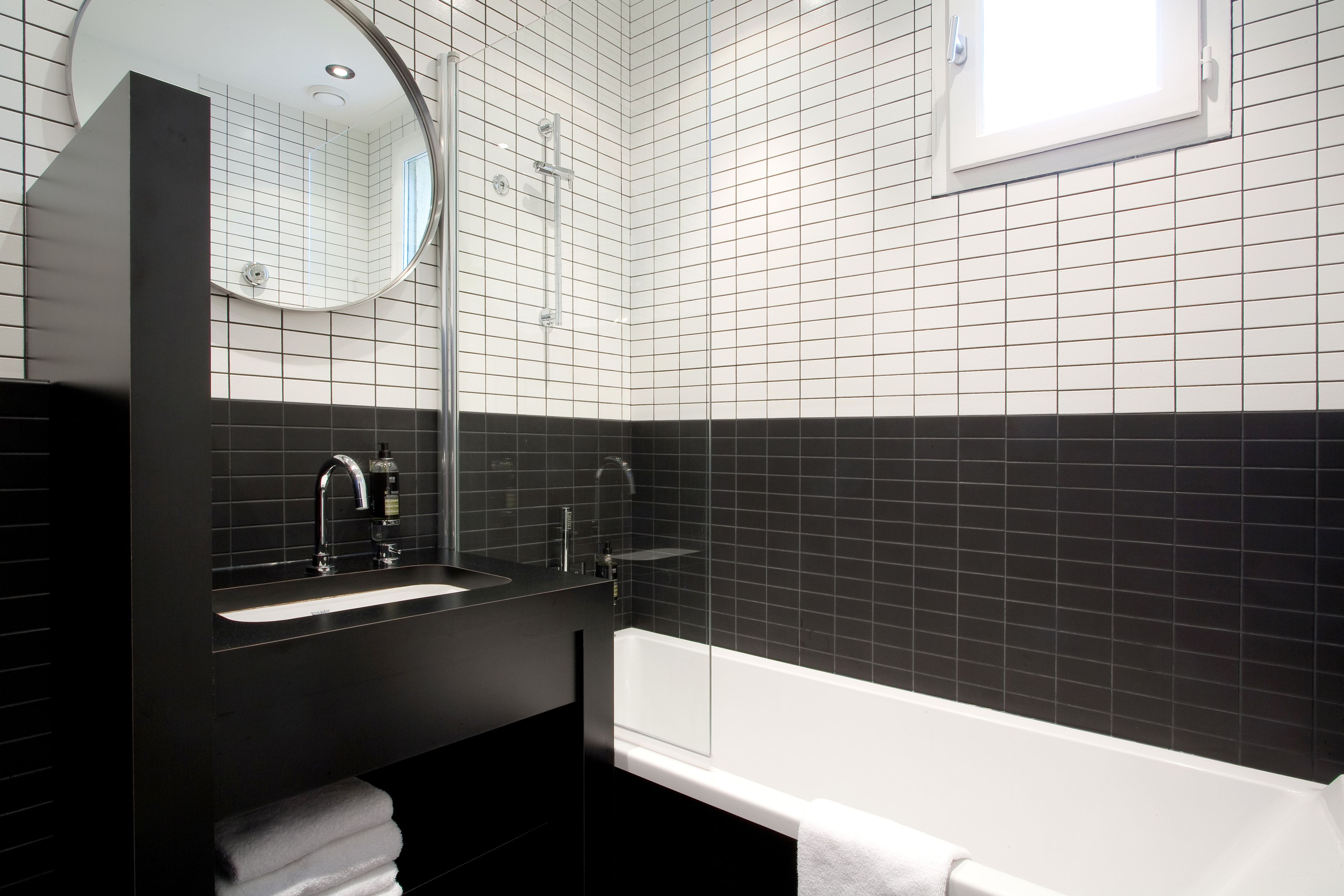 A modern bathroom with a black sink, mirror, and white bathtub.