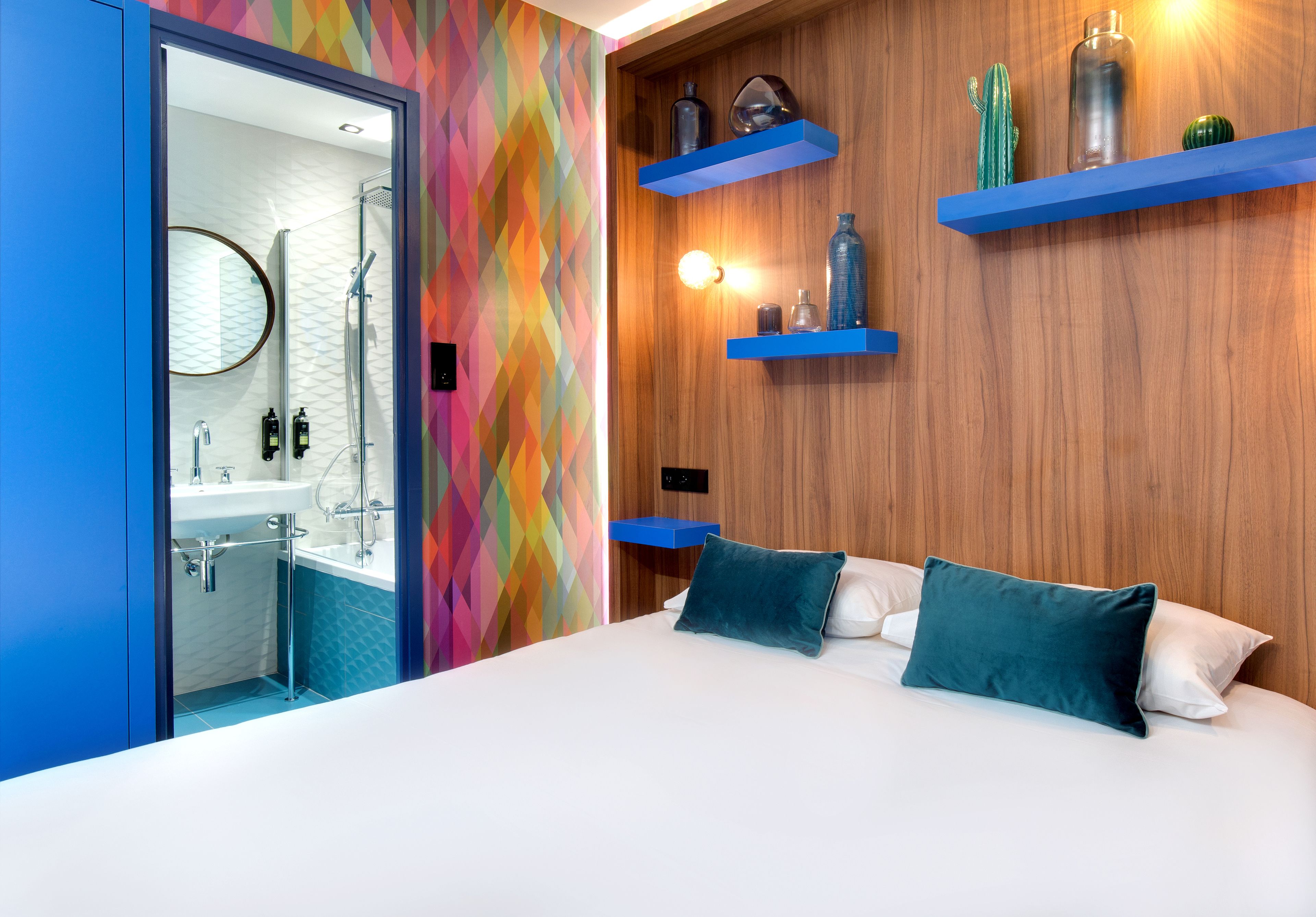 Ein modernes Schlafzimmer mit einem Bett, ein Badezimmer mit Dusche und blaue Regale mit Dekoration.