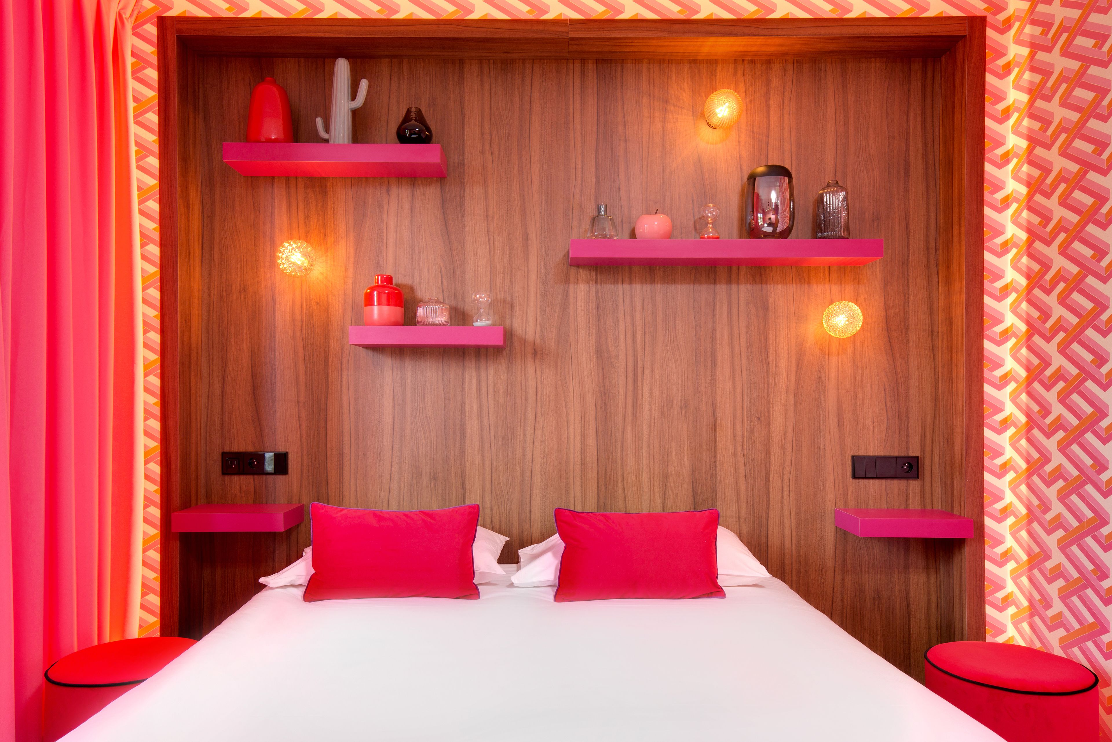 Ein Schlafzimmer mit einem Holz-Kopfteil, zwei roten Kissen, einer weißen Bettdecke und pinkfarbenen Regalen mit Dekoration.