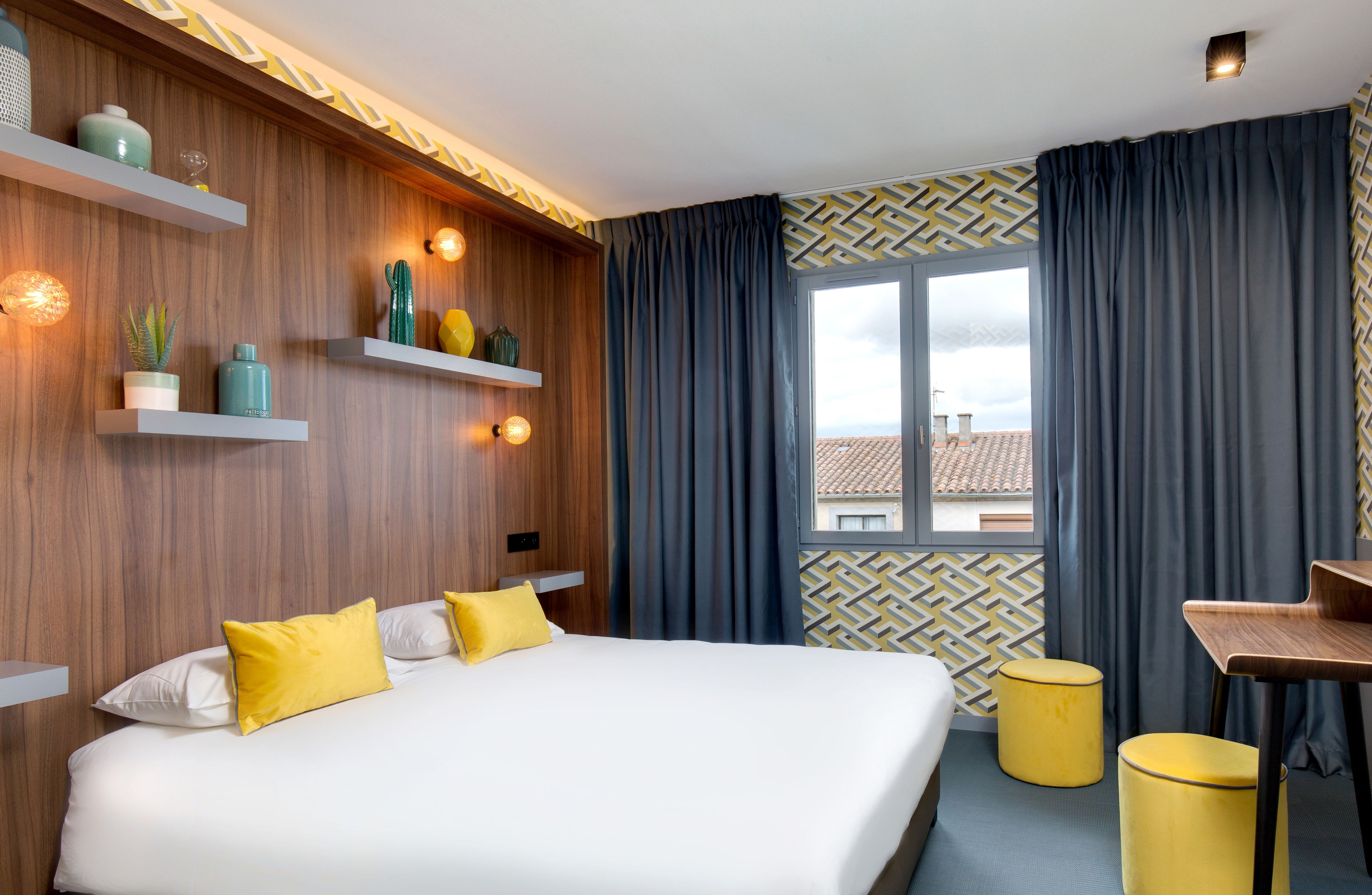 A hotel room with a large bed, a desk, and a window with curtains.