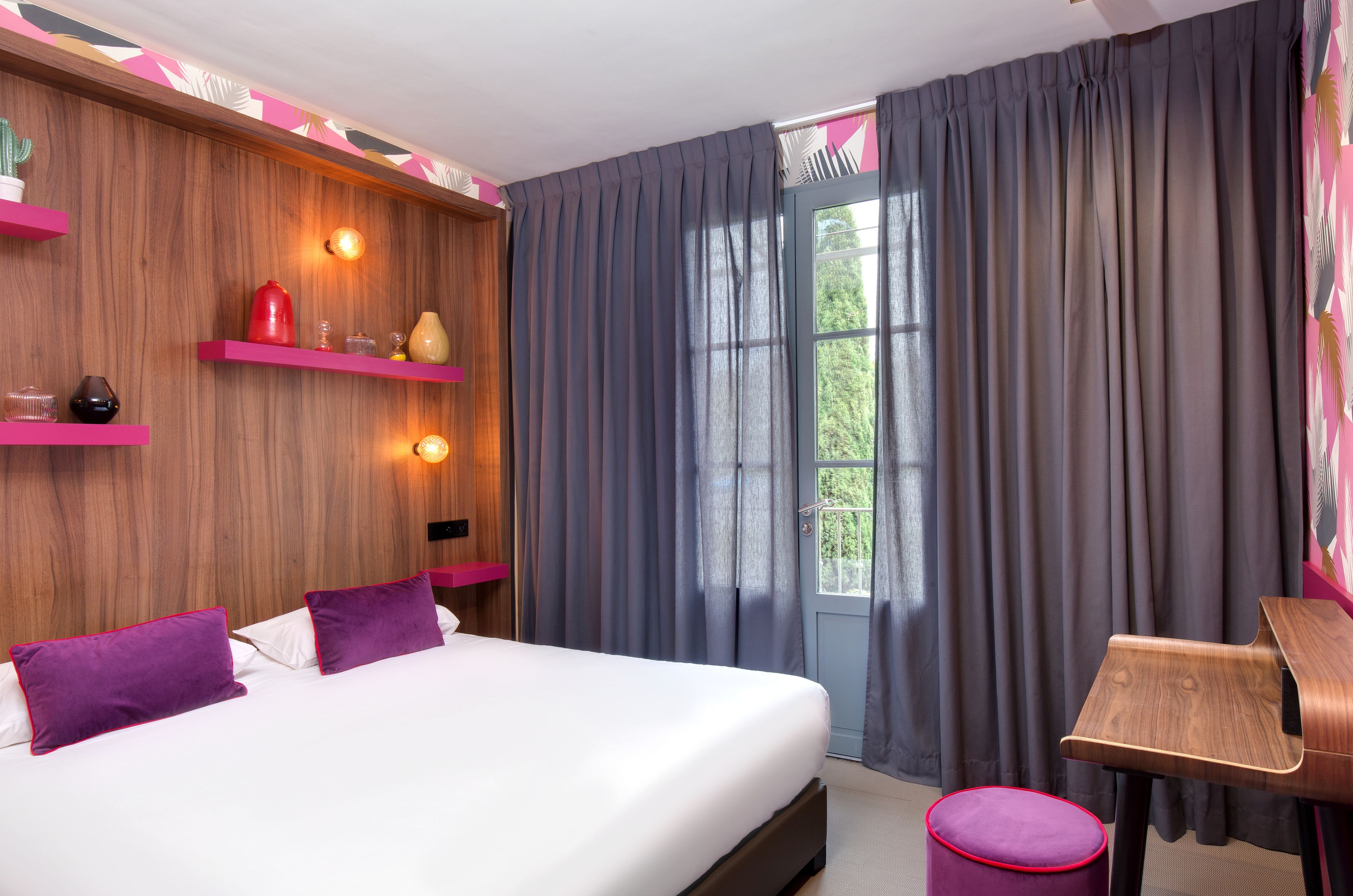 A modern hotel room with a wooden accent wall, a bed with white bedding, purple pillows, and a small wooden side table.