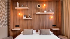 Un dormitorio moderno con cabecera de madera, dos mesitas de noche, una cama con dos almohadas y estantes en la pared con objetos decorativos.