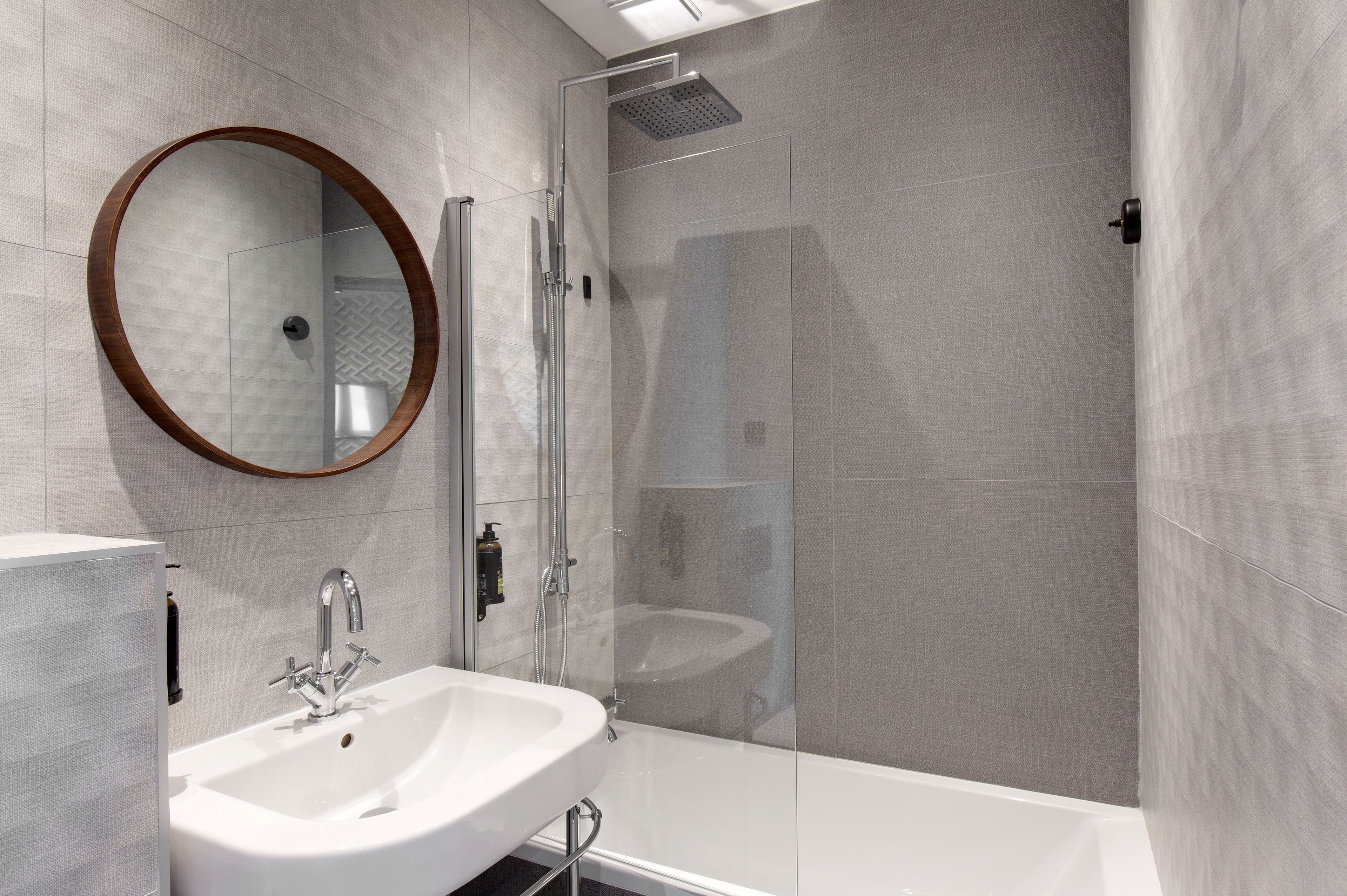 Une salle de bain moderne avec une douche à parois de verre, un miroir rond et un lavabo blanc.