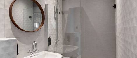 A modern bathroom with a glass-enclosed shower, a round mirror, and a white sink.