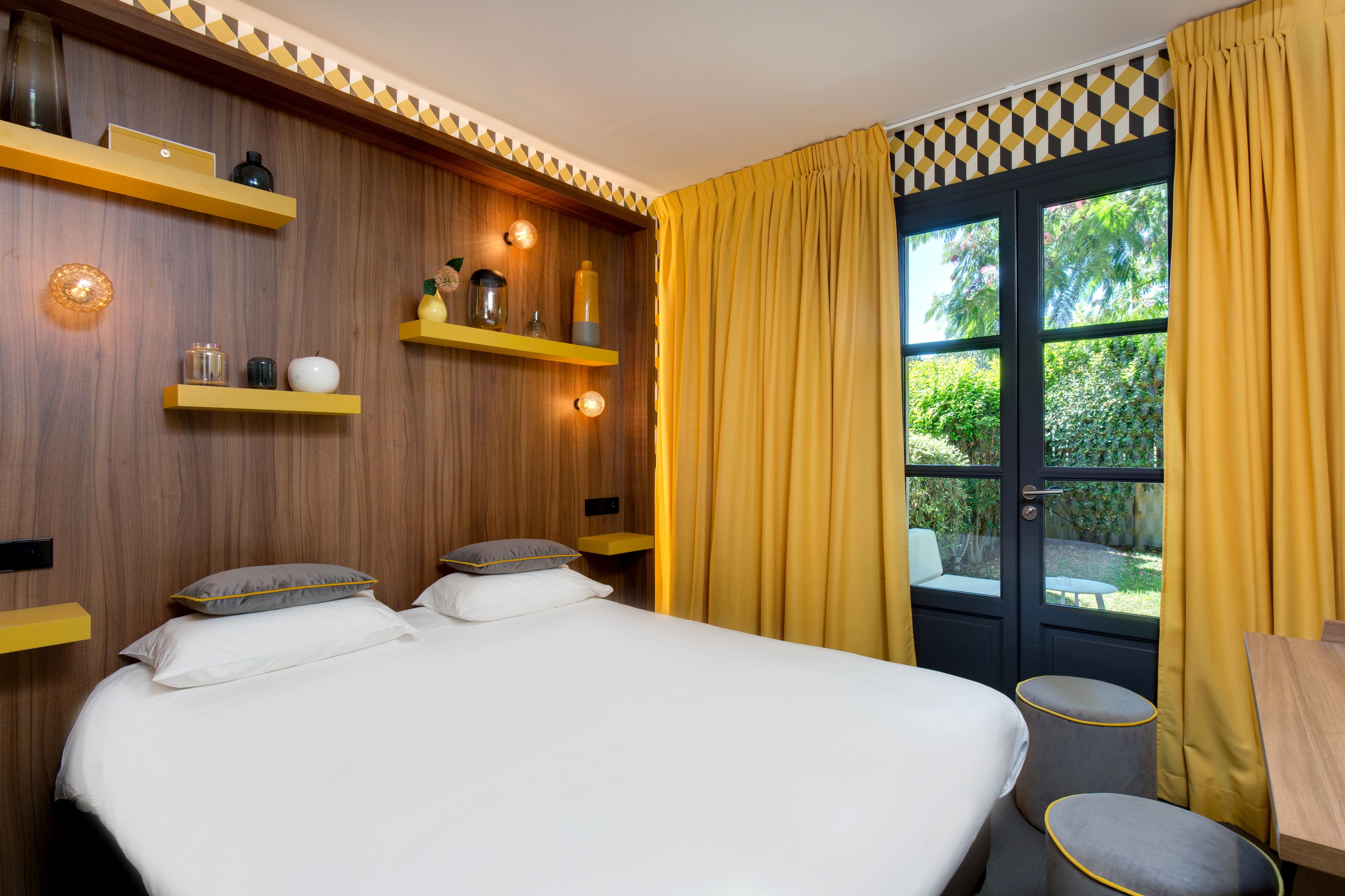 A bedroom with a bed, two bedside tables, a small round table, and a window with curtains.