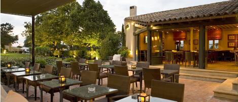 An outdoor patio with tables and chairs, a covered seating area, and a building with a tiled roof.