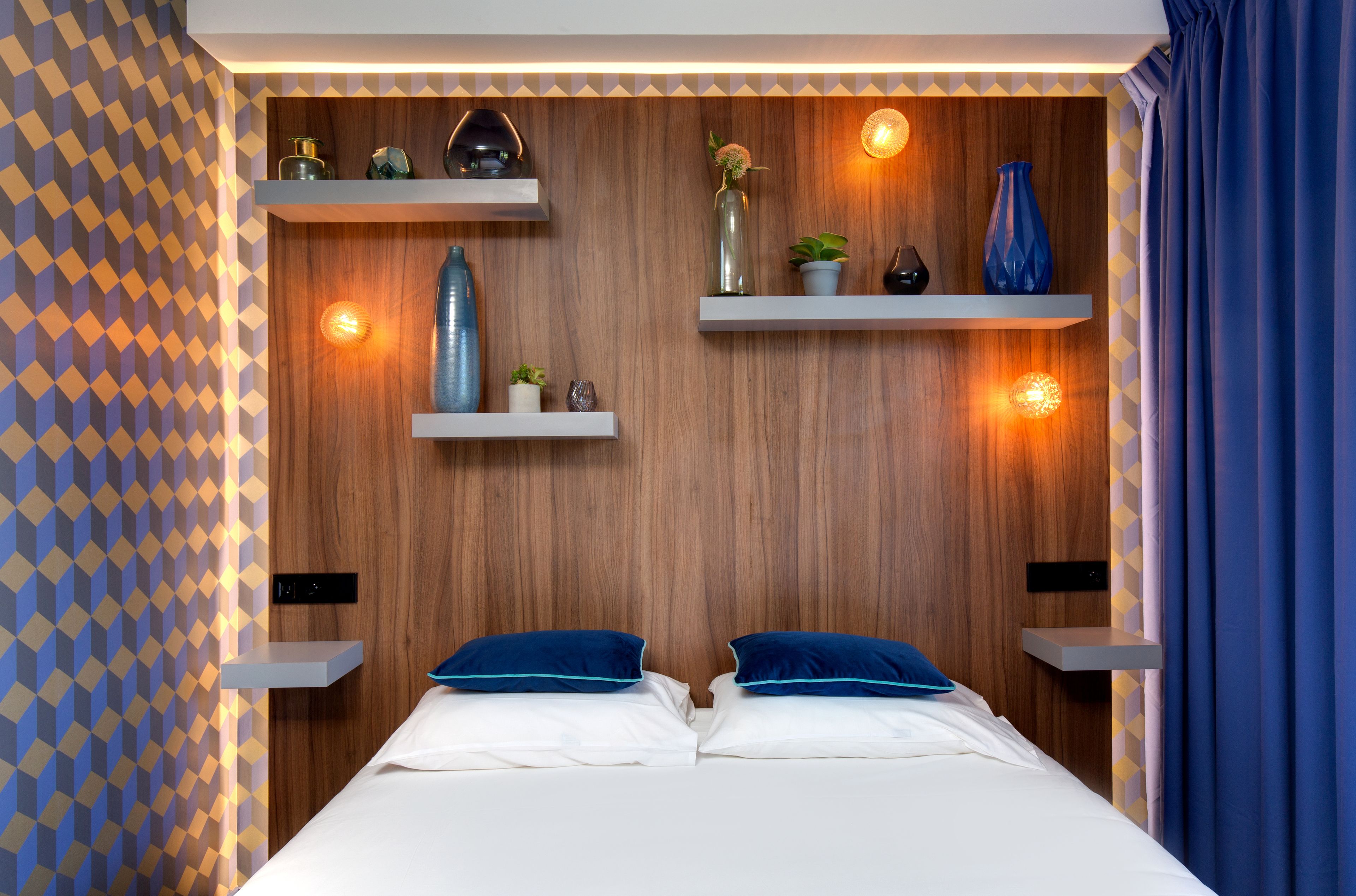 A modern bedroom with a wooden headboard, two bedside tables with decorative items, and a patterned wall.