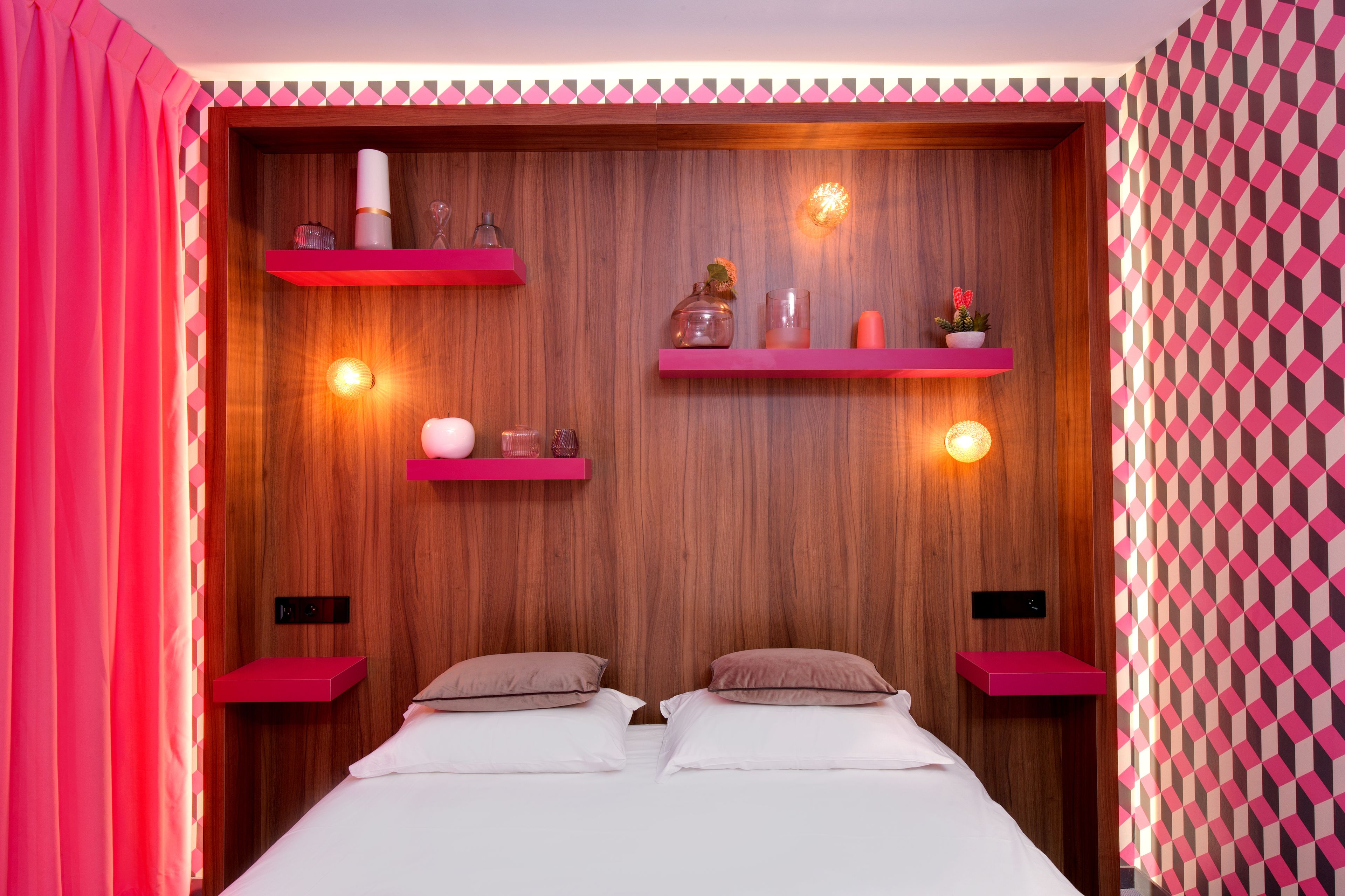 Ein Schlafzimmer mit Holz-Kopfteil, rosafarbenen Regaleinheiten und einer Wand mit Muster.