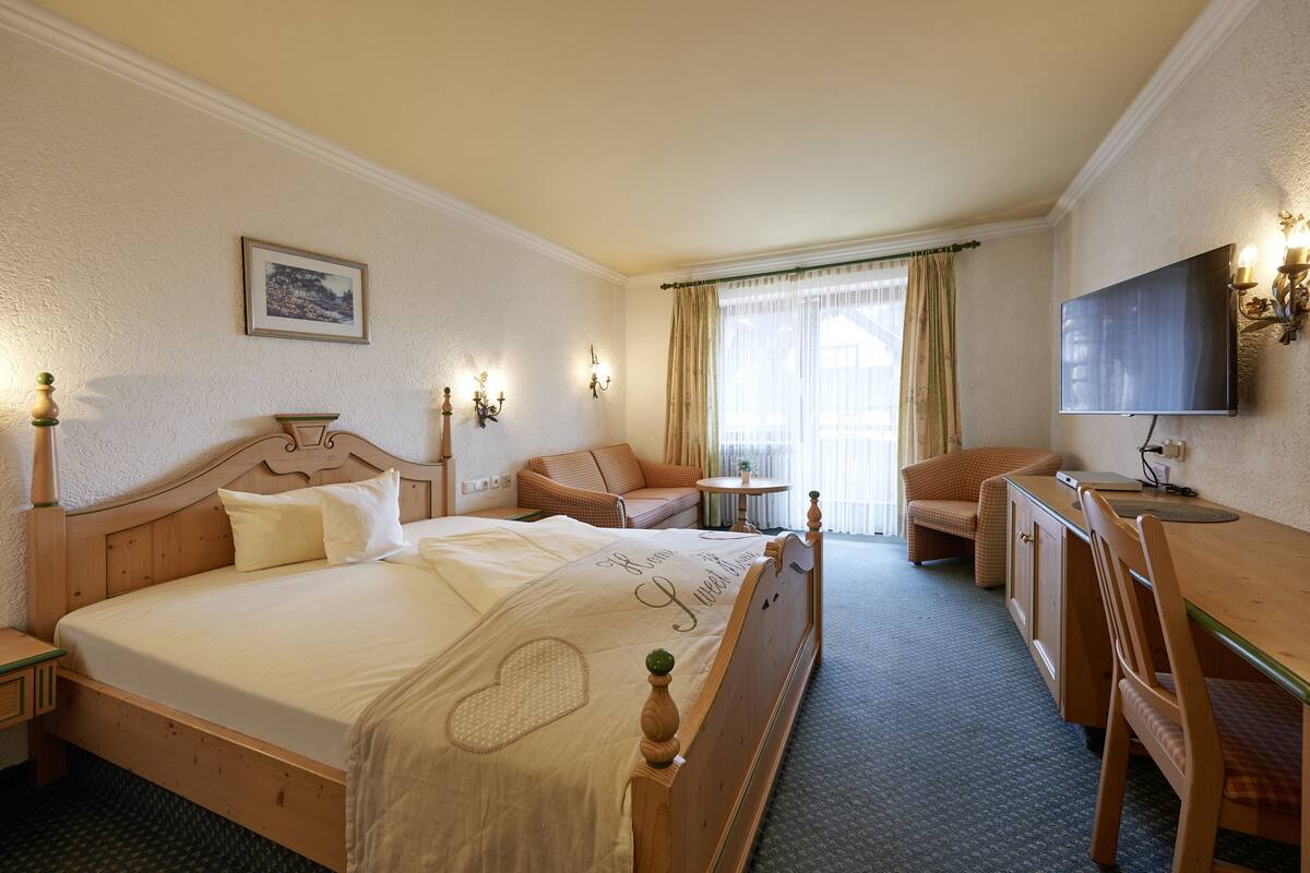 A hotel room with a large bed, a desk, a chair, a television, and a small table.