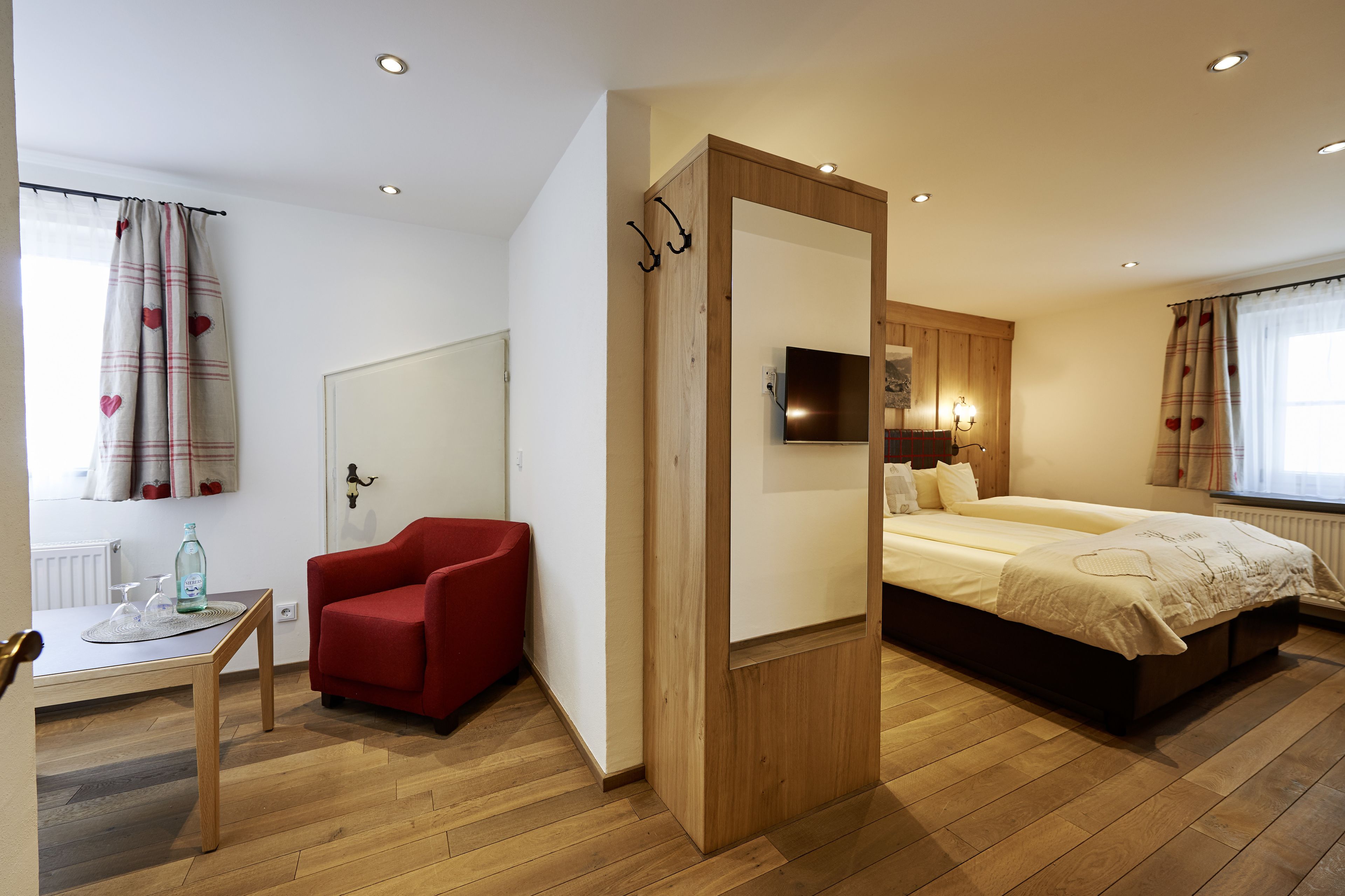 A bedroom with a bed, a red chair, a small table with a bottle, and a mirror.