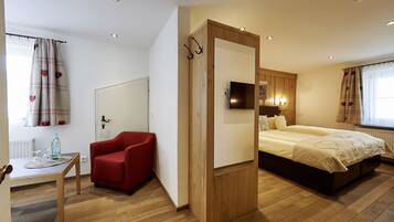 A bedroom with a bed, a red chair, a small table with a bottle, and a mirror.