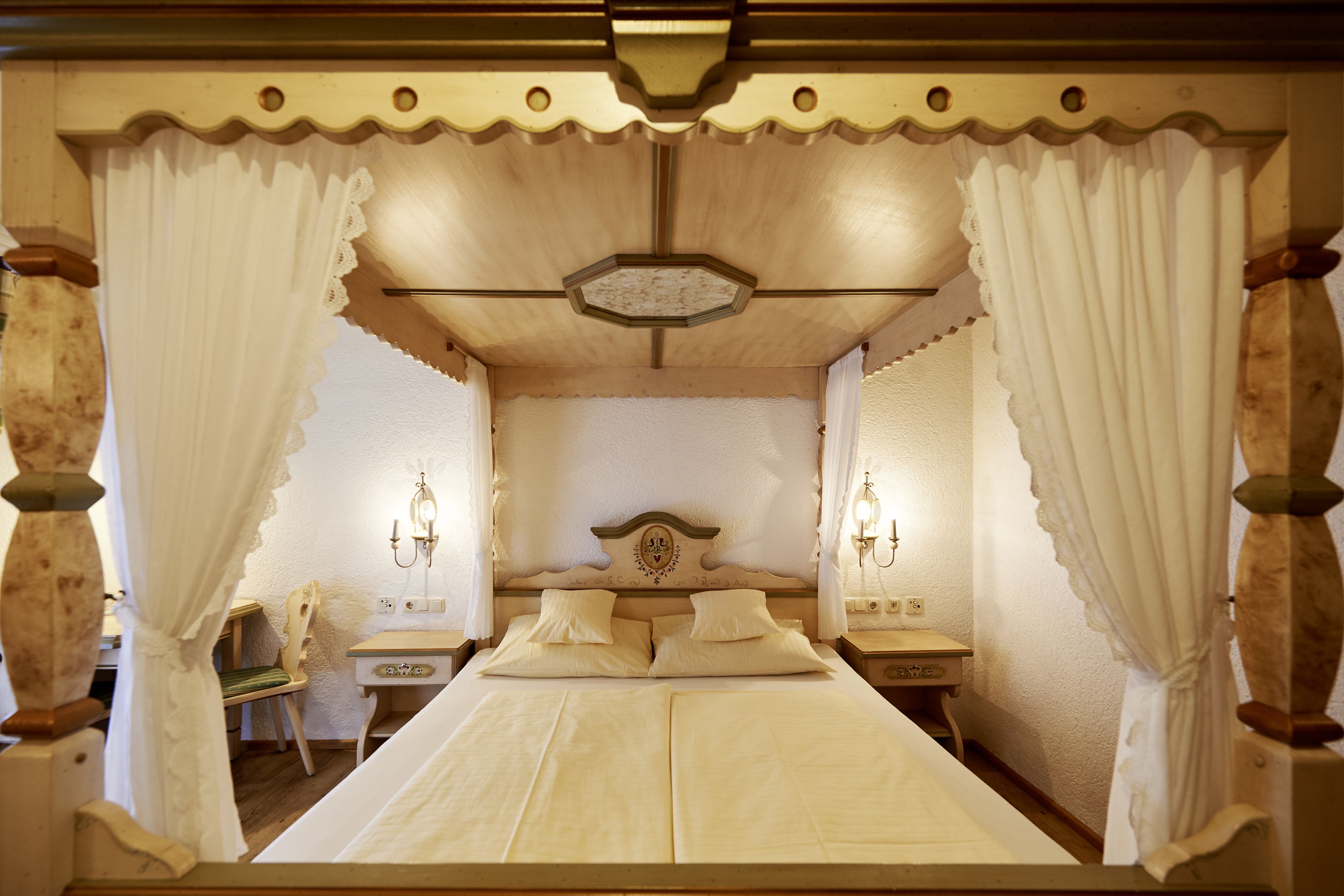 Una cama tradicional con dosel, un cabecero de madera, dos mesitas de noche y una silla.